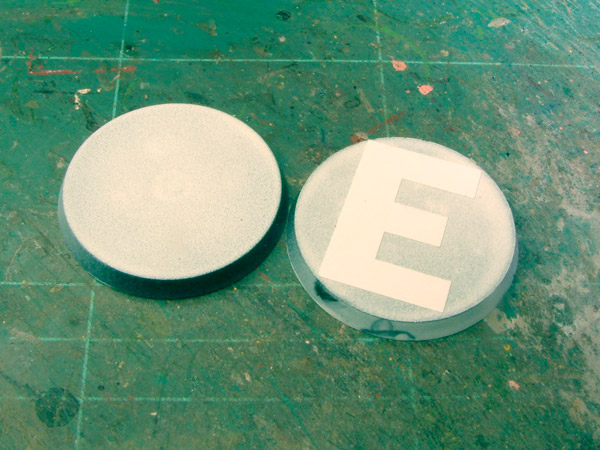 Two 40-mm bases painted white, one with a self-adhesive letter applied